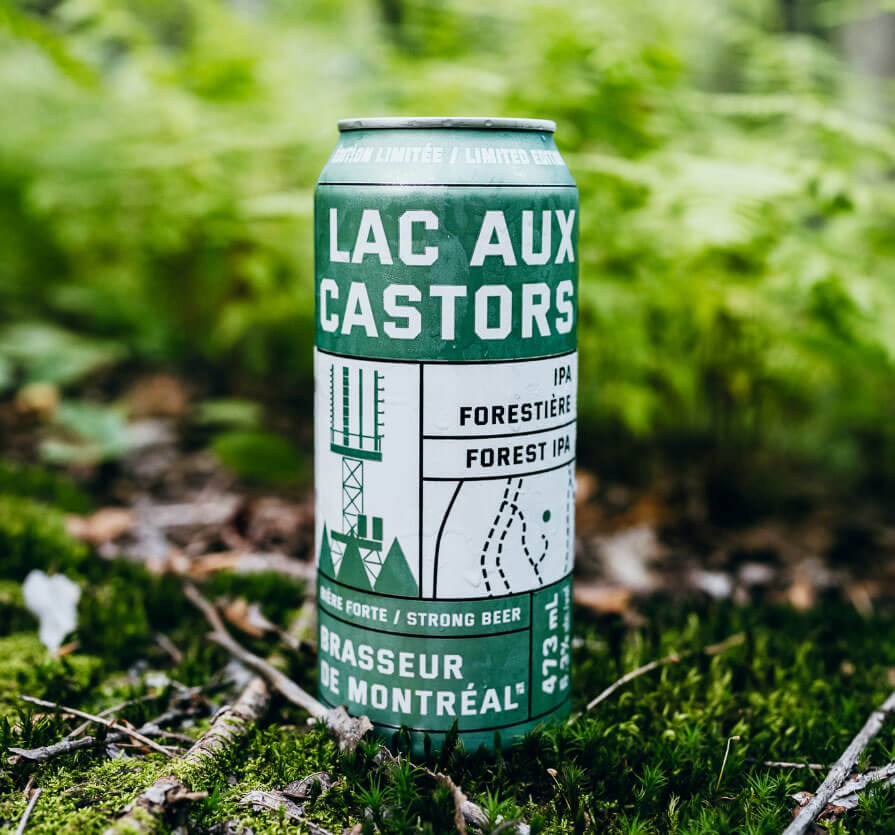 Green “Lac aux Castors IPA” beer can standing on mossy forest ground with blurred greenery in the background.